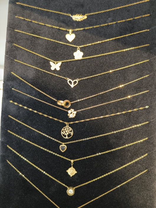 BIJOUX Présentation de bracelets dorés avec pendentifs variés sur un présentoir en velours noir.